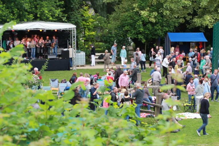 Besucher des Mittsommerfests in Holzhausen, vor einer Bühne mit Musikern und zahlreichen Sitzgelegenheiten.