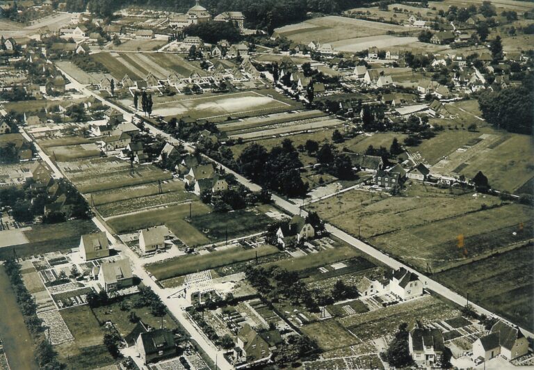 Alte Luftaufnahme von Holzhausen mit Feldern, Wohnhäusern und dem Kloster im Hintergrund.